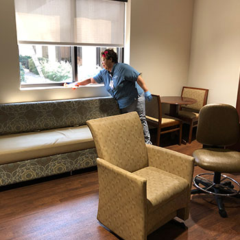 A member of the Enviornmental Services team wipes down a window in a patient room