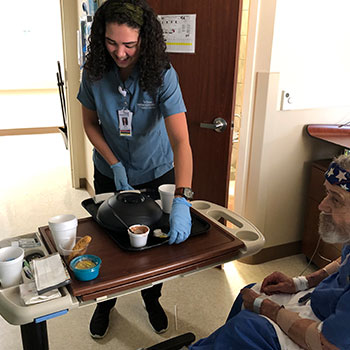 A woman laughs while cleaning the dishes from a patient meal